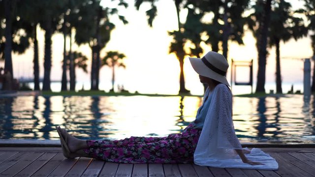 Lady holidaying at poolside with sunset in the background 