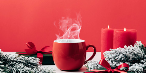 Winter or christmas cozy composition, steaming cup coffee or hot drink, Xmas decoration, branch fir, gift, on red background. Christmas, New Year, winter concept. Front view, copy space