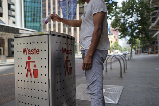 Recycle bin sign male Asian traveller dressing a white t- shirt, gray pant, standing placing empty aluminium cane drink bottle into waste bin