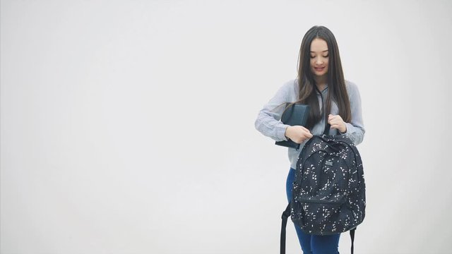 Asian girl with long hair appearing on a white background, hiding black book into her backpack and disappearing.