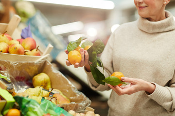 Cropped portrait of smiling senior woman choosing tangerines at fruit stand while shopping in...