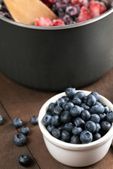 Ramekin of blueberries beside a saucepan of berries,  in a pie recipe scene 