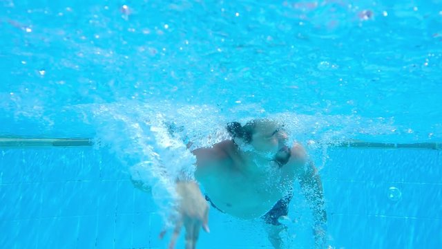 Man is dives and swimming underwater. Air bubbles float to surface of water pool. Underwater photography. Slow motion.