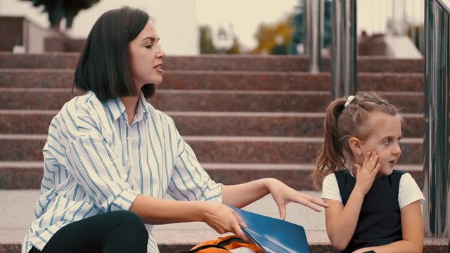 A mother and daughter are preparing for school classes. The parent and child are sitting on hte stairs and having a small talk.