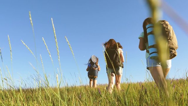 Teamwork travelers. travelers go with backpacks through meadow. mom and daughters, little baby travel across field with backpacks in colors in summer. Tourist girls and a little baby go camping .