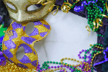 Mardis Gras border on marble background includes harlequin mask with green, gold and purple beads and matching fabrics. Copy space © Perry Correll