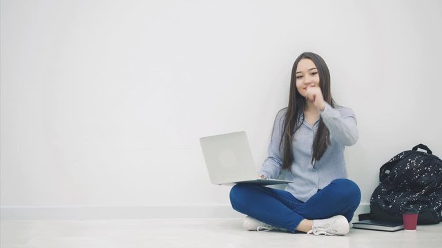 Lovely young asian lady sitting on the floor in lotos position, with laptop, looking to the side, giving thumb up, smiling.