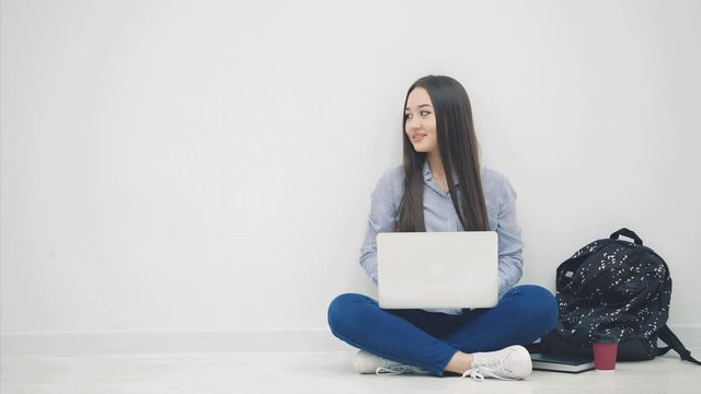 Lovely young asian lady sitting on the floor in lotos position, with laptop, looking to the side, giving thumb up, smiling.