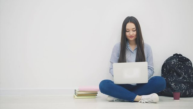 Young asian lady sitting on the floor in lotos position, searching something in her laptop, taking apple out from her bag, puttingit on the stack of books.
