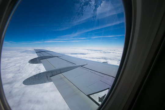 View from the window of the plane onto the wing and engines of a fokker 100 model with a blue sky and white clouds. Sunny weather