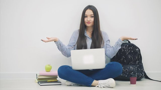 Young asian lady sitting on the floor in lotos position, with laptop, raising her hands with copyspace for text or product, weighting.