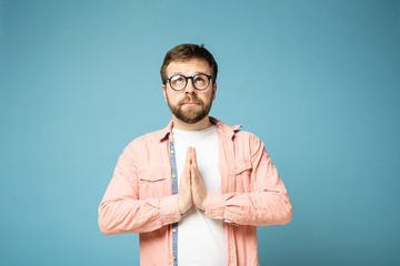Calm, bearded man with glasses, cupped palms together and looks up. Isolated on a blue background.