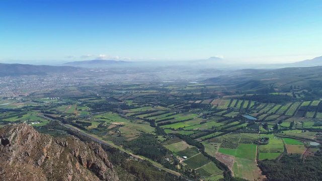 Aerial - Farms looking like stitched together patches, flying backwards revealing edge of mountain, blue clear sky