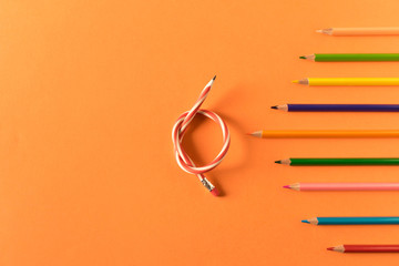 Colored pencils with one flexible pencil on orange background. The concept of flexibility in...