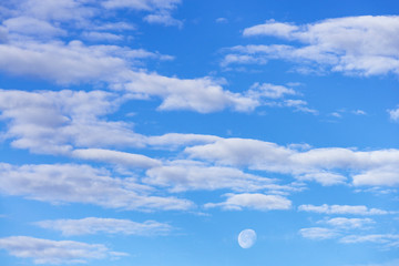 moon in a blue sky with white clouds