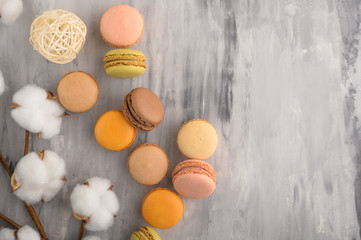 Colored french macaroons, sweets with cotton branches. On a marble background with space
