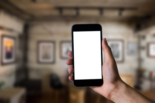 Mockup image of man's hands holding white mobile phone with blank screen in modern cafe.