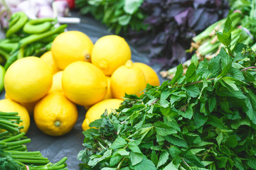 Close-up of fresh mint lying on the counter, against a background of bright lemons among different spices from herbs on the market.  Yellow lemon, basil, onion, fresh herbs. The concept of a healthy