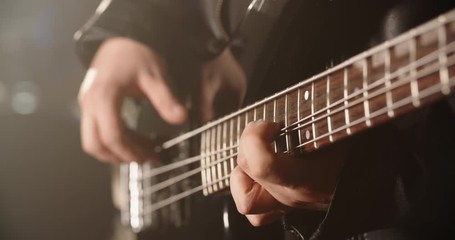A rock bass guitarist is playing a solo line during performance in club, band mate drummer hitting cymbals on background 4k footage
