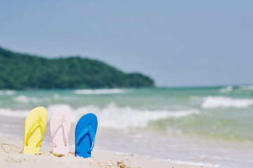 Three flip-flops on the sunny tropical beach, sea waves in background
