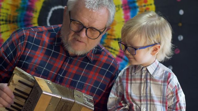 blond child and father with gray hair and beard in plaid shirts celebrate together family holiday. Father plays the accordion while boy holds a microphone. Lovely family duet