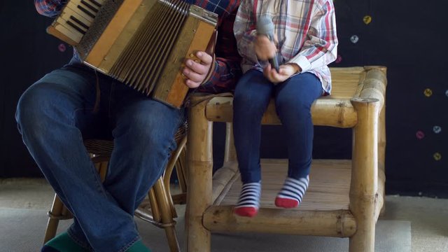 blond child and father with gray hair and beard in plaid shirts celebrate together family holiday. Father plays the accordion while boy holds a microphone. Lovely family duet