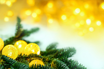 Fototapeta na wymiar Festive Christmas composition of Christmas tree branches and. Teclichny glowing balls garlands on a background of blurry yellow lights,copy space