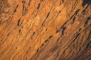 Sunny nature background of rockies in sunlight. Vivid natural mountain texture of big rough rocks. Full frame of bright giant craggy surface. Rocky mountain close-up. Plane of shiny rocks on sunset.