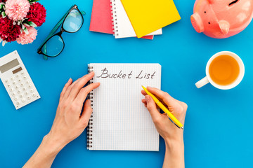 Bucket list. Blank notebook to write goals and wishes - with women hands - on blue office desk top-down mockup
