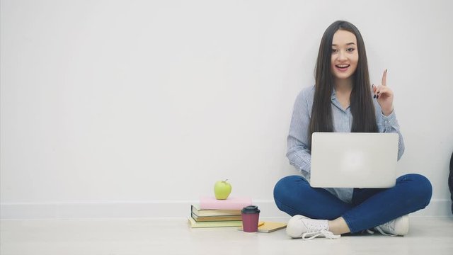 Young asian female student sitting in lotos position, using laptop, pointing her finger up as if coming up with excellent idea, then pointing finger forward.