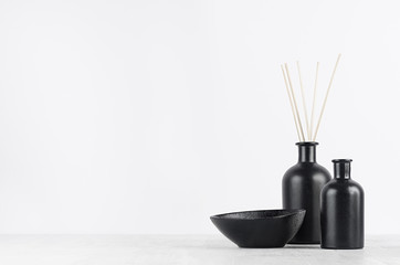 Aromatherapy black bottles with sticks and decorative bowl on soft light white table with copy space as elegant home decor for holiday.