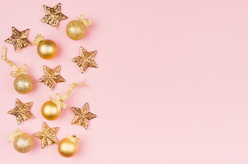 Christmas background - golden stars and sparkling glittering balls on soft light pastel pink background, border, copy space, top view.