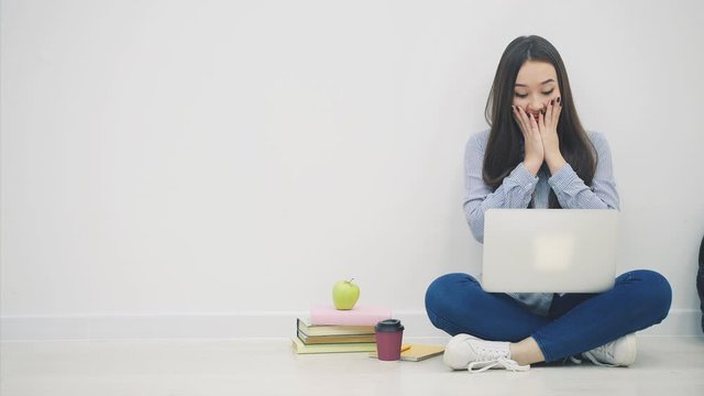 Lovely young asian lady searching something in her laptop. Surprised by something, covering her mouth, pointing finger up as if calling to pay attention, then point to the copyspace.