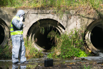 a specialist in a gray protective suit and mask, on the pond, calls the mobile phone to the management to report the results of the study
