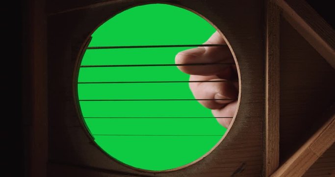 From the inside of a guitar fingers plucking low sounding strings