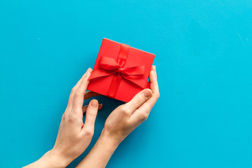 Give a gift on Valentine's Day. Women hand hold beautiful red present box on blue background top-down copy space
