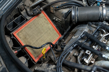 Close-up on a dirty air filter for an engine with an orange frame installed in the engine compartment of a premium car during vehicle maintenance in auto service industry and vehicles