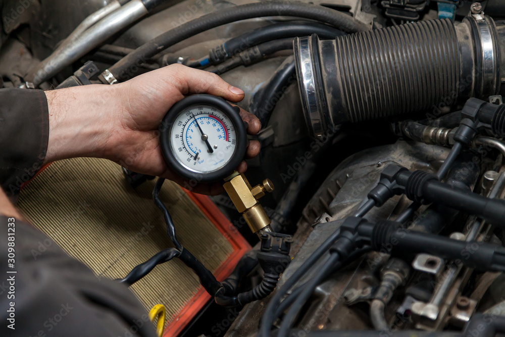 Fototapete a male mechanic measures the compression in the cylinder of a car engine using a barometer with a sc