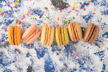French macaroons in a row of colored, on a colored background with colored caramel sweets.