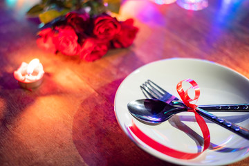 Romantic dinner valentines day love concept - valentines table setting decorated with fork spoon on white plate and roses flower bouquet with candlelight on wooden table dinner at night