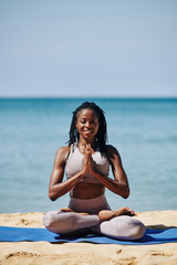 Fototapeta na wymiar Smiling young slim woman in lotus position strain outdoors with hands in master gesture and looking at camera