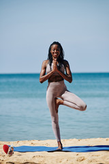 Happy young slim Black woman standing in tree asana and holding hands in namaste gesture