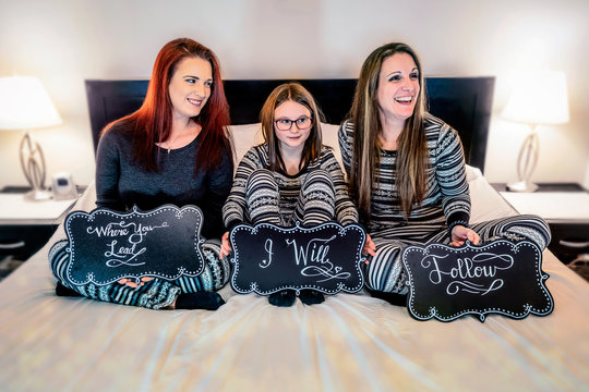 A Family Of Women Sitting On A Bed Wearing Matching Pajamas.