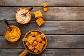 Prepare salted caramel. Scoop with sweet cubes, melted caramel and salt on dark wooden background top view copy space