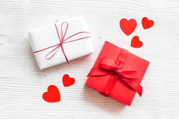 Present to a lover on Valentine's Day. Gift boxes near paper hearts on white wooden background top-down.