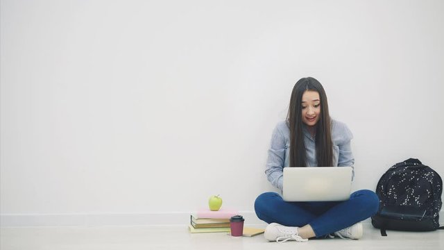 Asian lady sitting on the floor in lotos position, with laptop, raising up her hands, pointing at something very pleasant for her in the laptop, smiling happily as a winner.