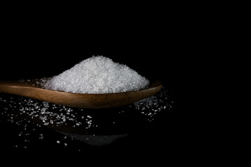 sugar in wooden spoon on dark background