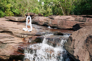 Beautiful young woman sitting by waterfall and enjoying meditation in nature