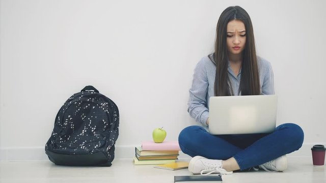 Lovely young asian lady sitting, with laptop, has some difficulties, clenching and shaking her fists, putting hands on the head. Cheerless face expression.