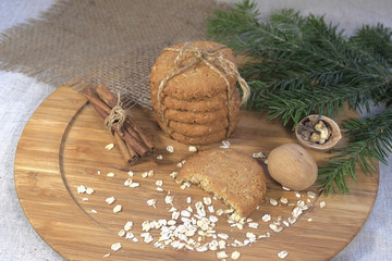 Homemade oatmeal cookies, oats, nuts, cinnamon sticks on a brown light wooden table. green spruce...